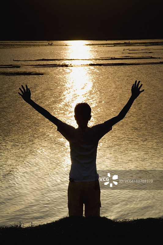 孩子在河边向天空伸展双臂图片素材