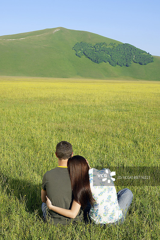 年轻情侣坐在山地，背影。图片素材