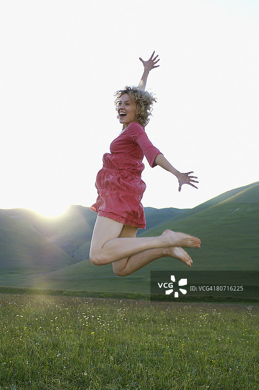 在山地草甸上喜悦跳跃的女人侧视图图片素材