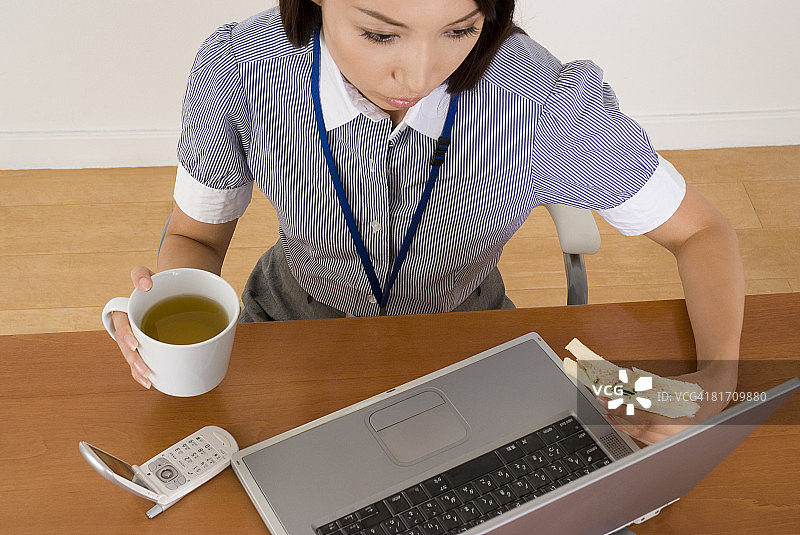 年轻女人在办公桌前吃三明治图片素材