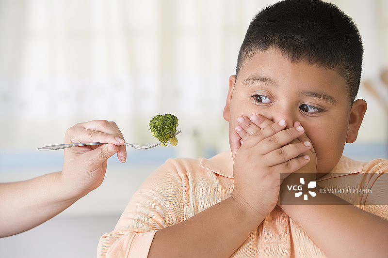 在西兰花旁边捂住嘴巴的西班牙裔男孩图片素材