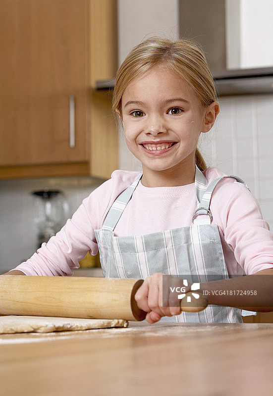 在厨房里用擀面杖擀面团并微笑的年轻女孩图片素材