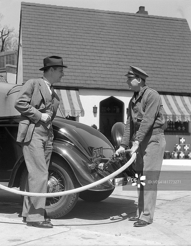 加油站服务员为轿车油箱加油，顾客微笑观看图片素材