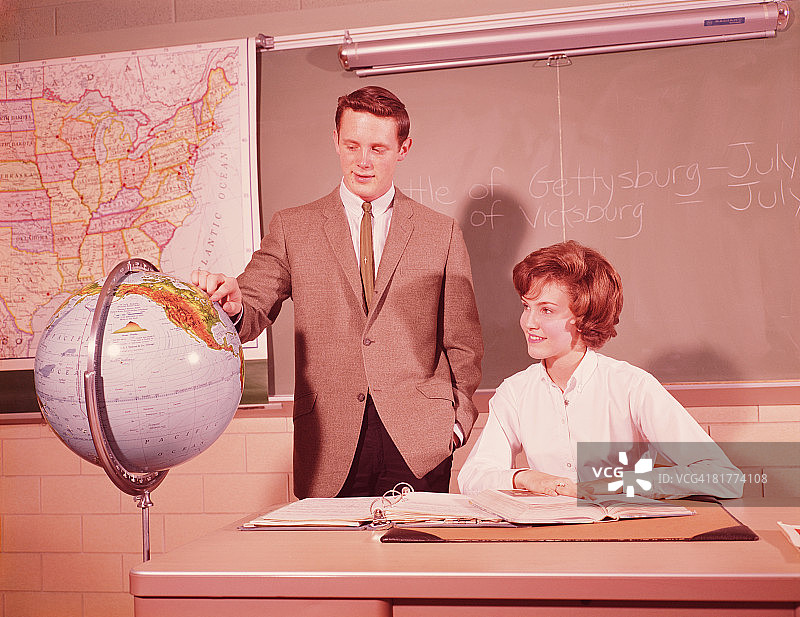 两名男生站在世界地球仪旁，女生坐在教室的课桌旁图片素材