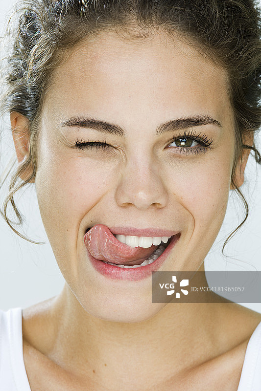 年轻女人眨眼并舔嘴唇的肖像图片素材