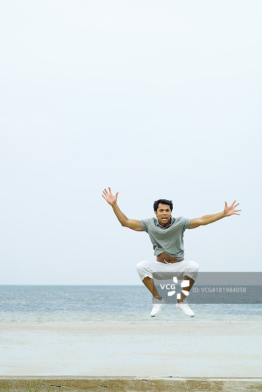 男人在海滩上跳跃，张开双臂，看向镜头图片素材