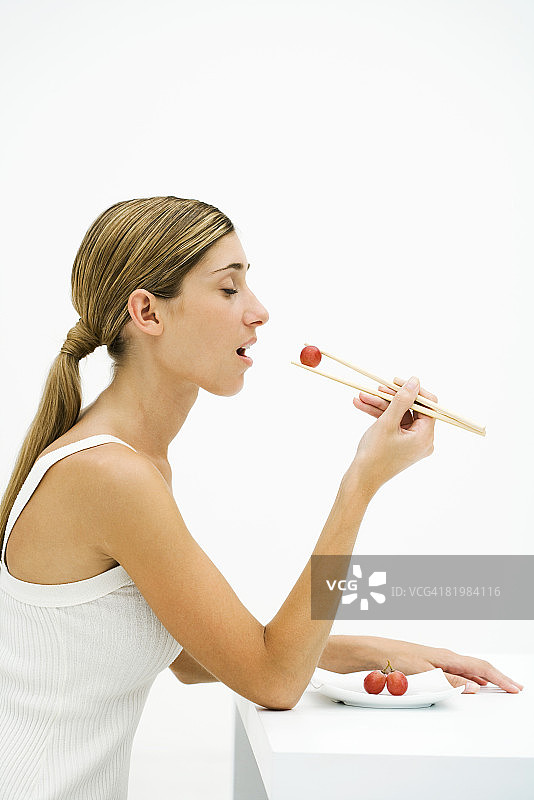 女人用筷子吃红色葡萄（闭眼，侧视）图片素材
