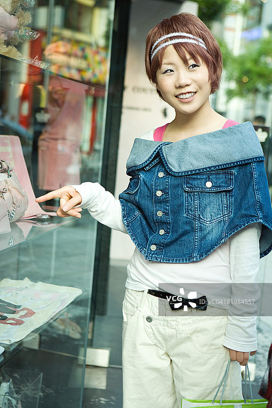 年轻女子在橱窗购物，指点并看向别处图片素材