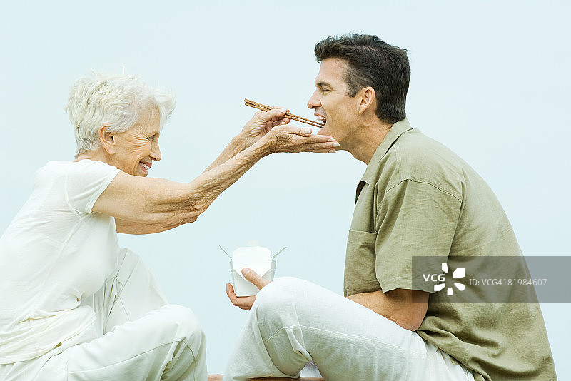 年长的女性用筷子喂成年儿子外卖食物，侧视图图片素材