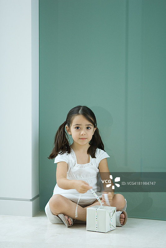 坐在地上系礼物丝带，看着镜头的小女孩图片素材