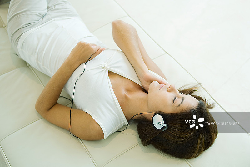 年轻女子仰卧戴耳机闭目听音乐图片素材