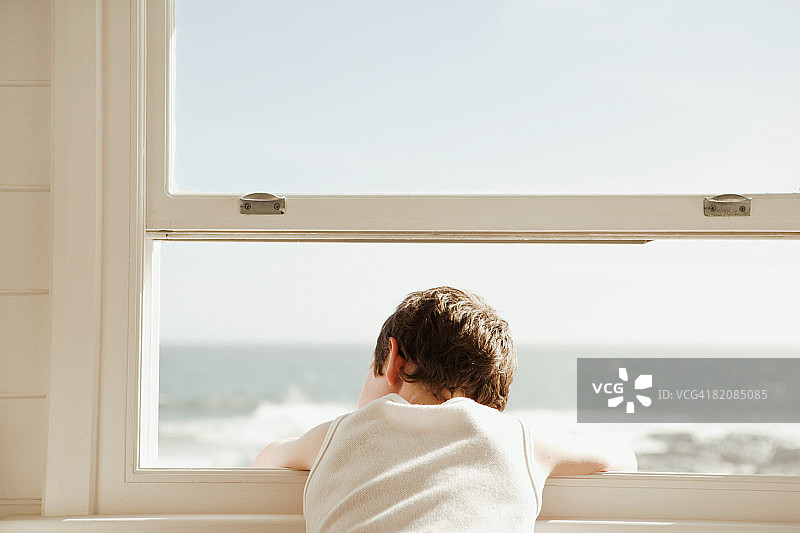 男孩在海滩小屋的窗户向外看图片素材