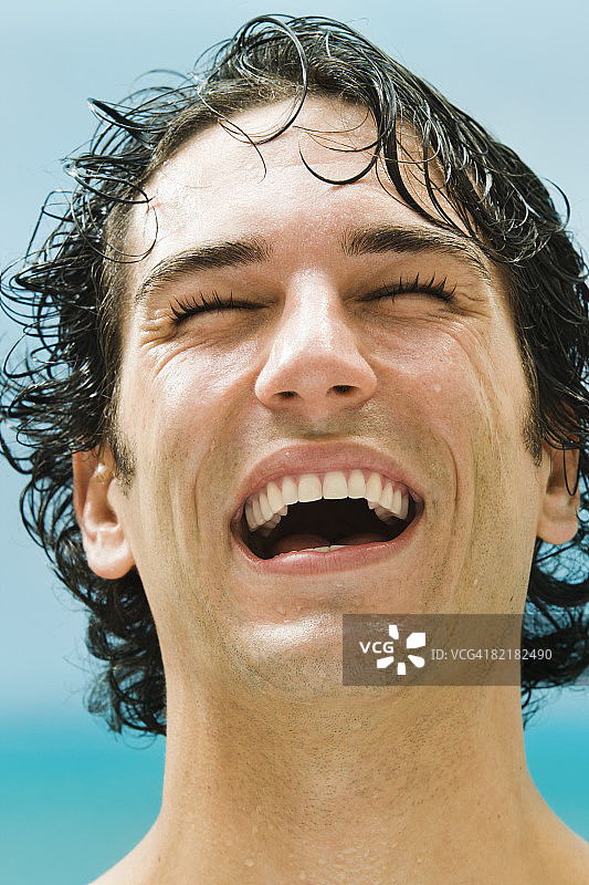 海滩上闭着眼睛大笑的男人肖像图片素材