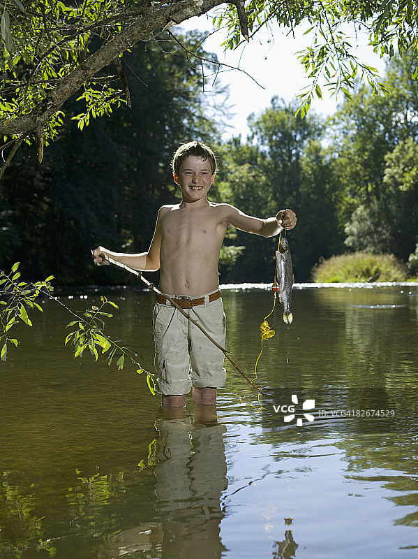 男孩站在河里拿着鱼，笑着图片素材