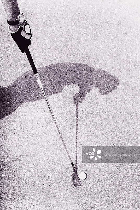 高尔夫球手持球杆站在球旁，绿地上有阴影（黑白）图片素材