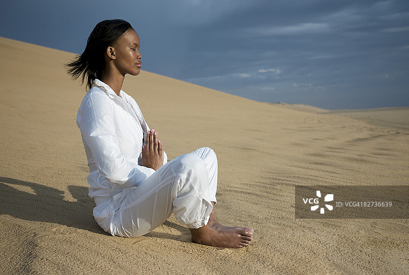 年轻女子坐在沙丘上冥想图片素材