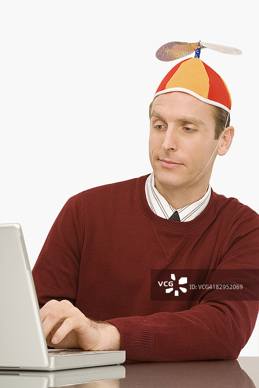 商人戴着螺旋桨小帽在笔记本电脑上工作图片素材