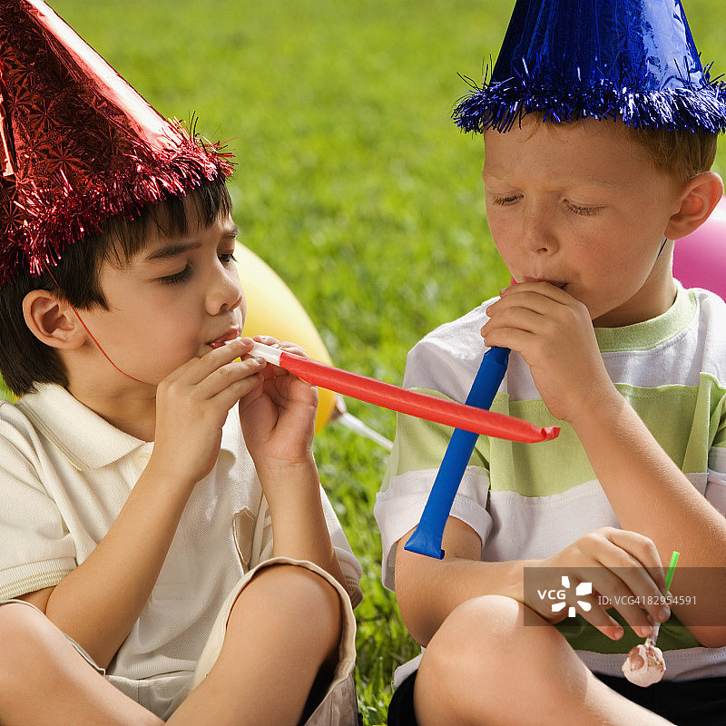 两名男孩坐在一起吹派对喇叭图片素材