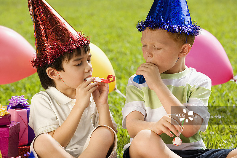 两名男孩坐在一起吹派对喇叭图片素材