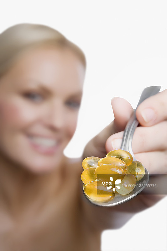 年轻女人展示勺子里维生素药丸的特写图片素材