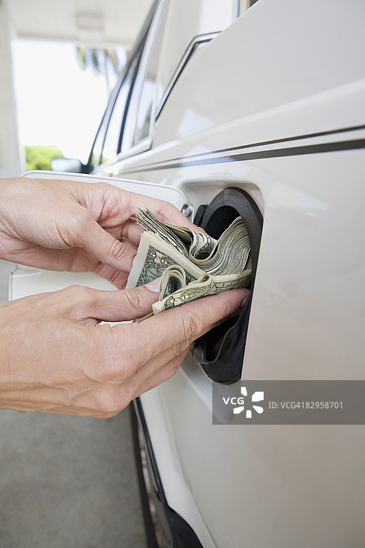 特写：一人将美元纸币放入汽车油箱图片素材