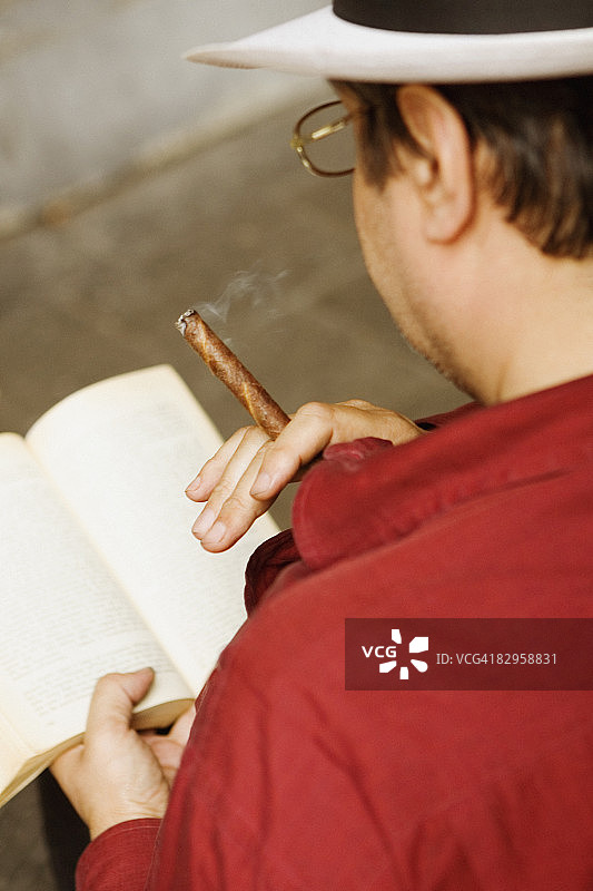 男子在意大利热那亚东方市场哥伦布广场读书和抽雪茄的背面图片素材