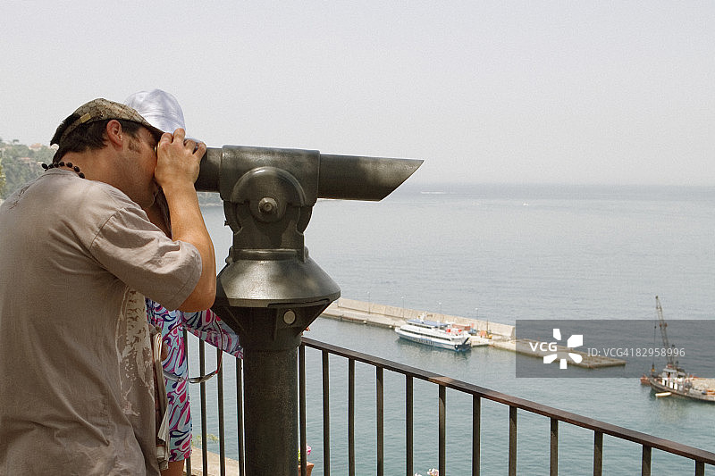 男人在那不勒斯索伦托使用投币式望远镜的侧面照图片素材