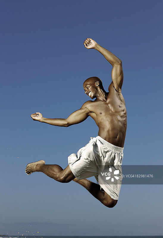 在海滩上跳跃，举起双臂的男人图片素材