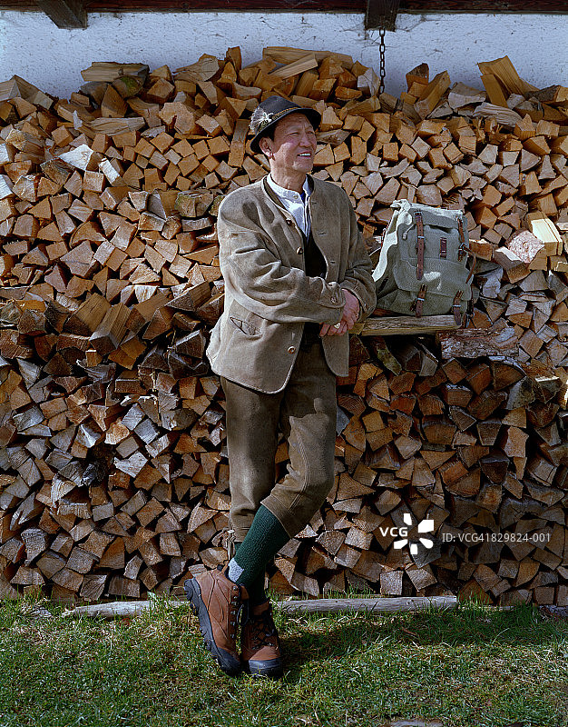 戴着羽毛帽、站在木柴前的男人图片素材
