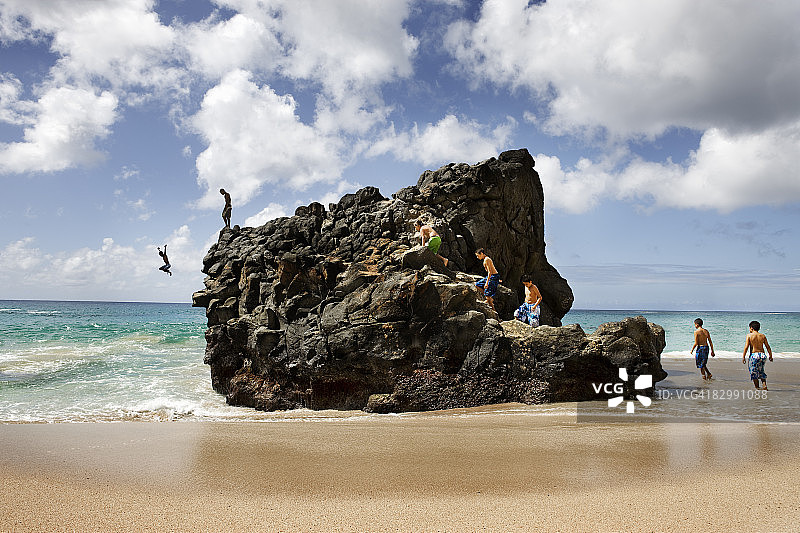 朋友攀爬岩石跳入大海图片素材