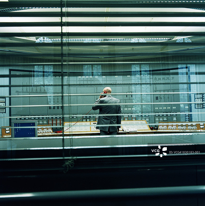 控制室里打电话的男人，透过窗户和百叶窗的后视图图片素材