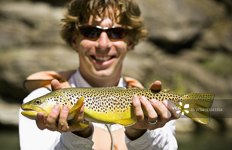 微笑著手持虹鳟鱼的男人图片素材