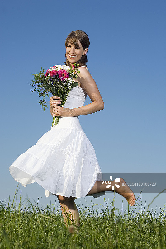 德国巴伐利亚：草地上手捧鲜花的微笑年轻女子图片素材