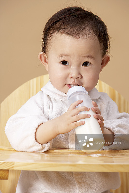 坐在高脚椅上用奶瓶喝水的女婴图片素材