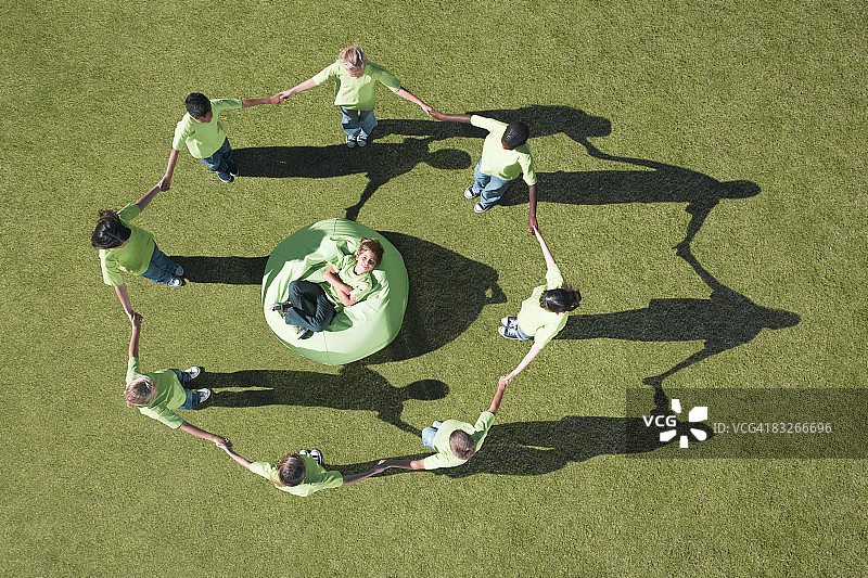 一群孩子手拉着手围着豆袋里的男孩图片素材