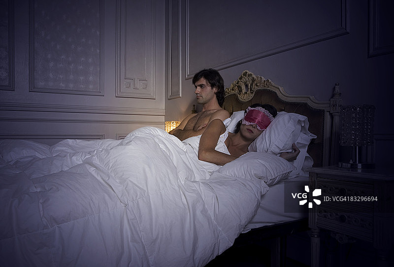 男人醒着，伴侣戴着眼罩睡觉图片素材