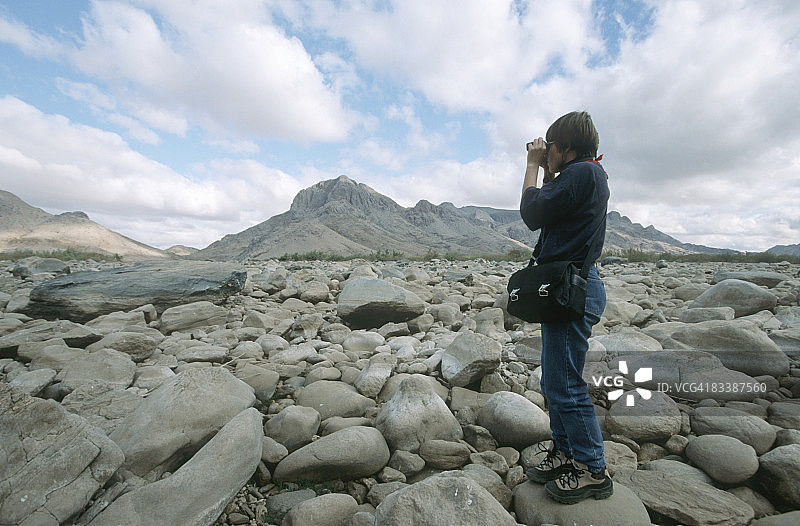 女子在南非北开普省佩拉的岩石河床上用双筒望远镜观察图片素材