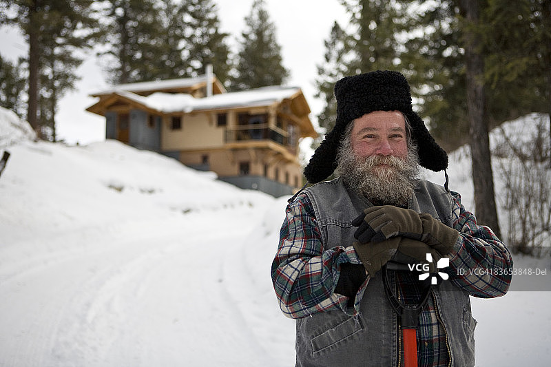 冬季在蒙大拿州怀特fish的房子前拿着雪铲的蓄须男人图片素材