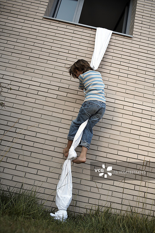 男孩用床单绳索爬出窗外图片素材