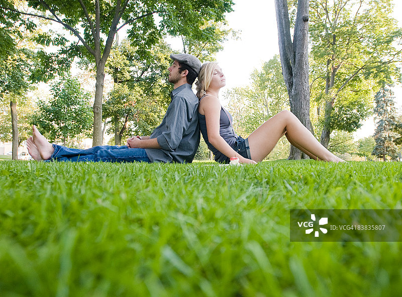 年轻情侣在公园里背靠背休息图片素材