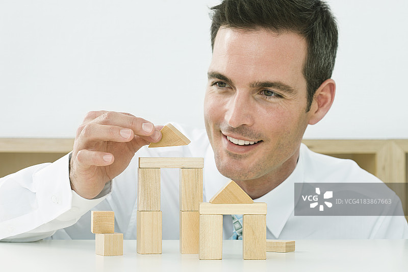 男人用木块搭建房屋，面带微笑图片素材