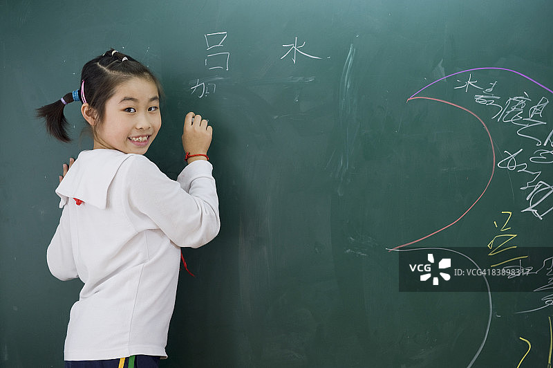 一个年轻学生在黑板上涂鸦。图片素材