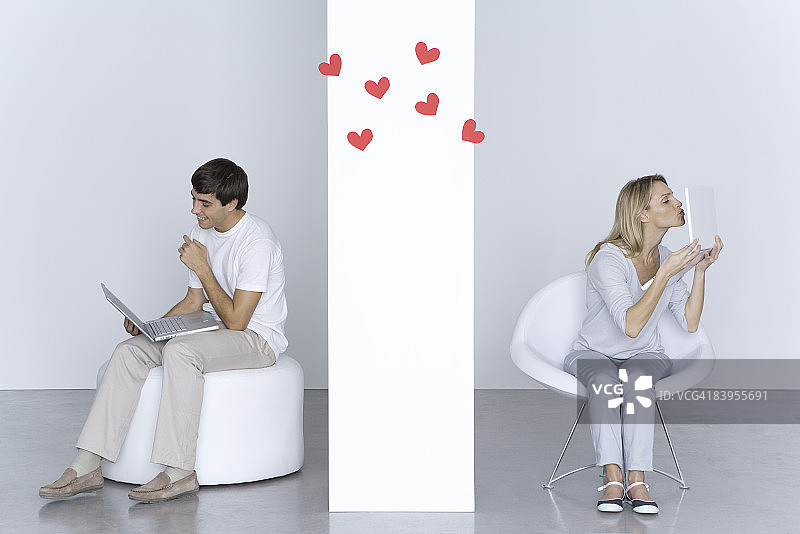女人亲吻笔记本电脑，男人看着自己的电脑微笑，两人之间有心形图案图片素材