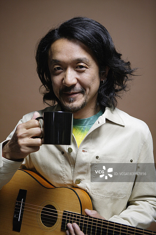 手持吉他和马克杯的中年男人特写肖像，影棚拍摄图片素材
