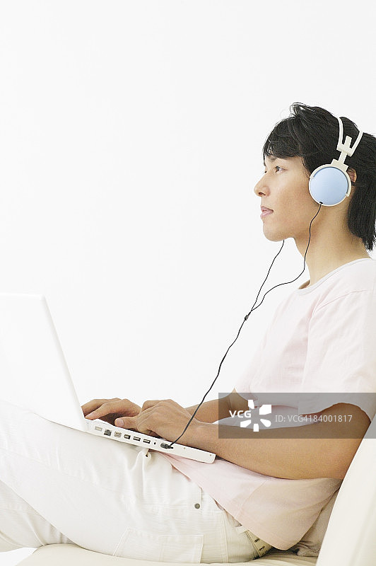 男人戴耳机坐在沙发上使用笔记本电脑图片素材