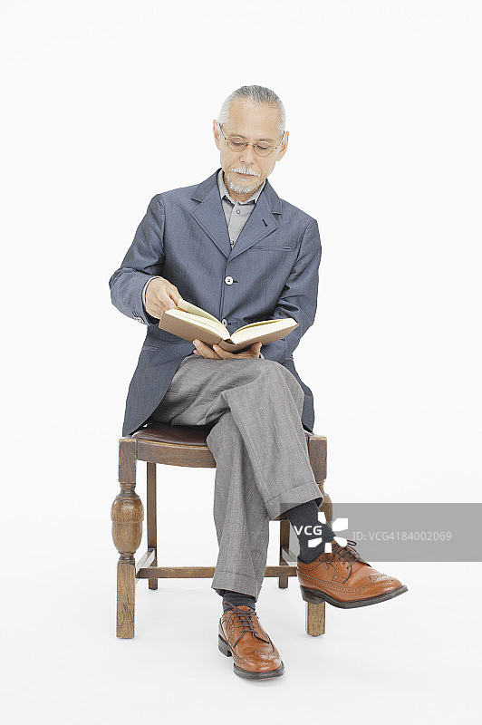 在椅子上看书的老年男人，影棚拍摄图片素材