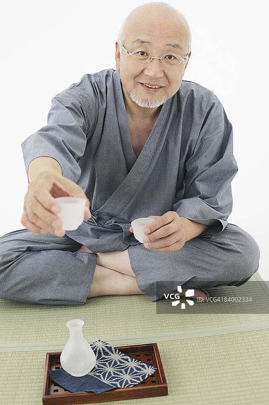 年长的男人手持小酒杯喝清酒，影棚拍摄图片素材