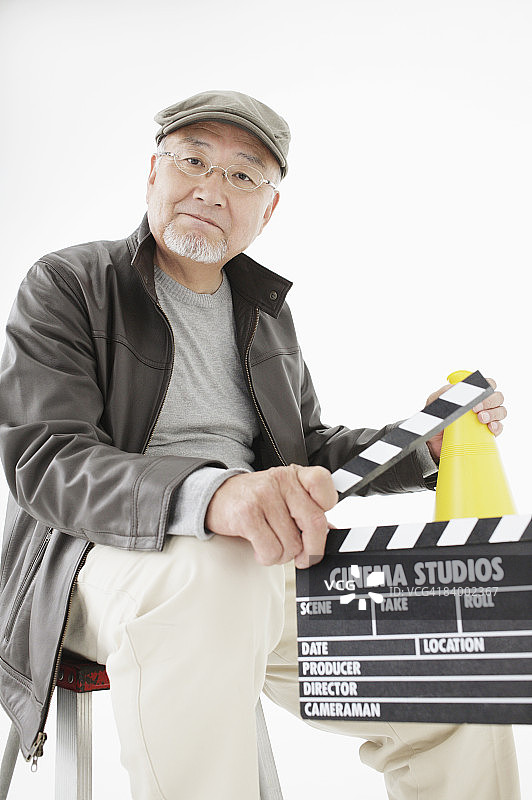 电影导演坐在椅子上，拿着扩音器和场记板的肖像，工作室拍摄图片素材