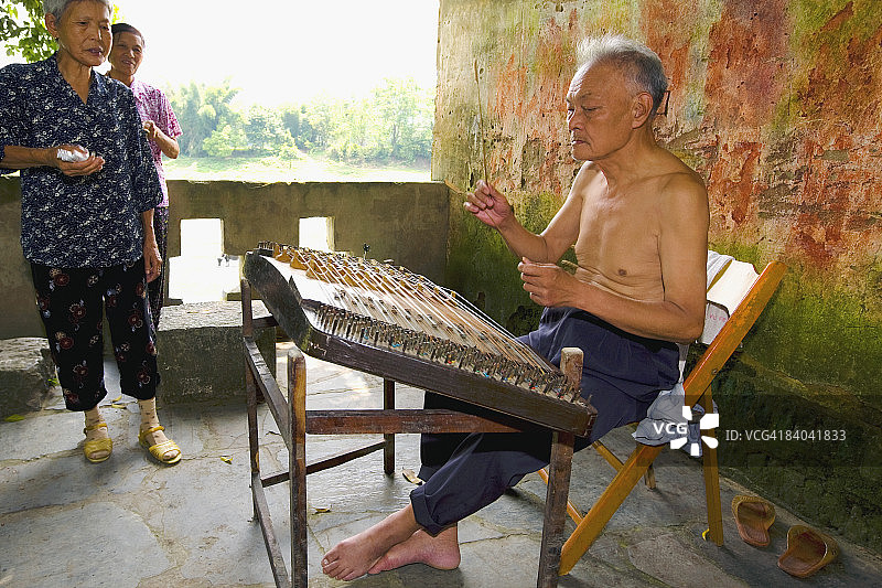 年长的男人和家人在旁演奏扬琴，中国广西阳朔福利村图片素材