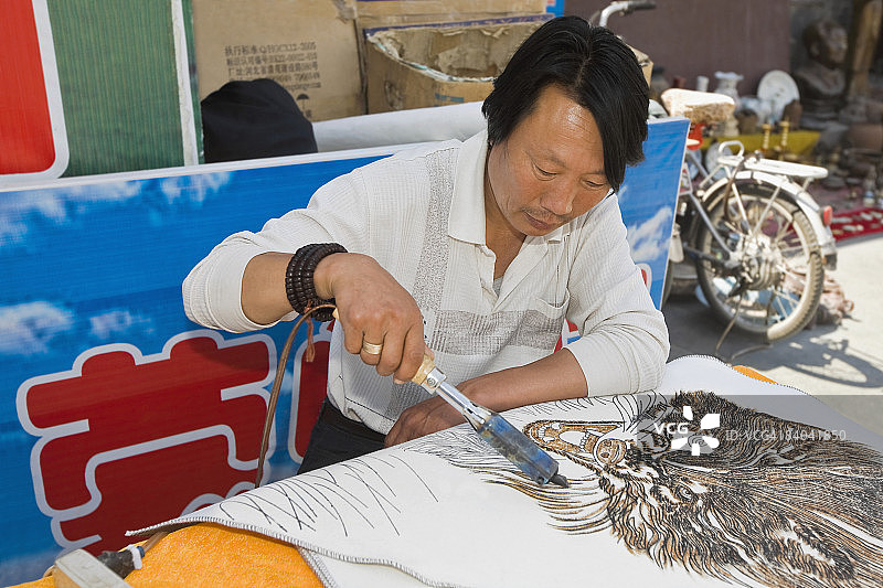 中国内蒙古呼和浩特，用烙铁在布上绘画的中年男人图片素材